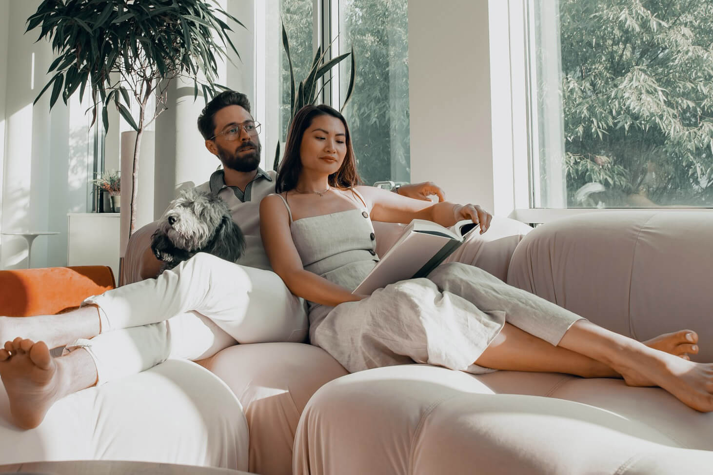 Couple pieds nus détendu sur un canapé, la femme lit pendant que son compagnon caresse leur chien, illustrant la tranquillité offerte par une intervention CRELEC HVAC Solutions